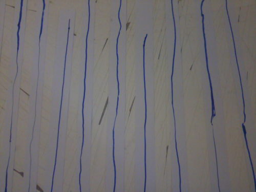 Sur une table striée de passages au cutter, des bandes blanches ornées de lignes bleues sont disposées simplement